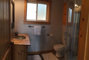 Ein Badezimmer mit Holzwaschtisch, Fenster, Toilette und Duschkabine aus Glas.