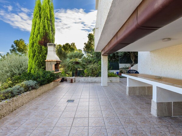 Relax on the spacious patio with a long bench, surrounded by lush greenery and a natural tree canopy.