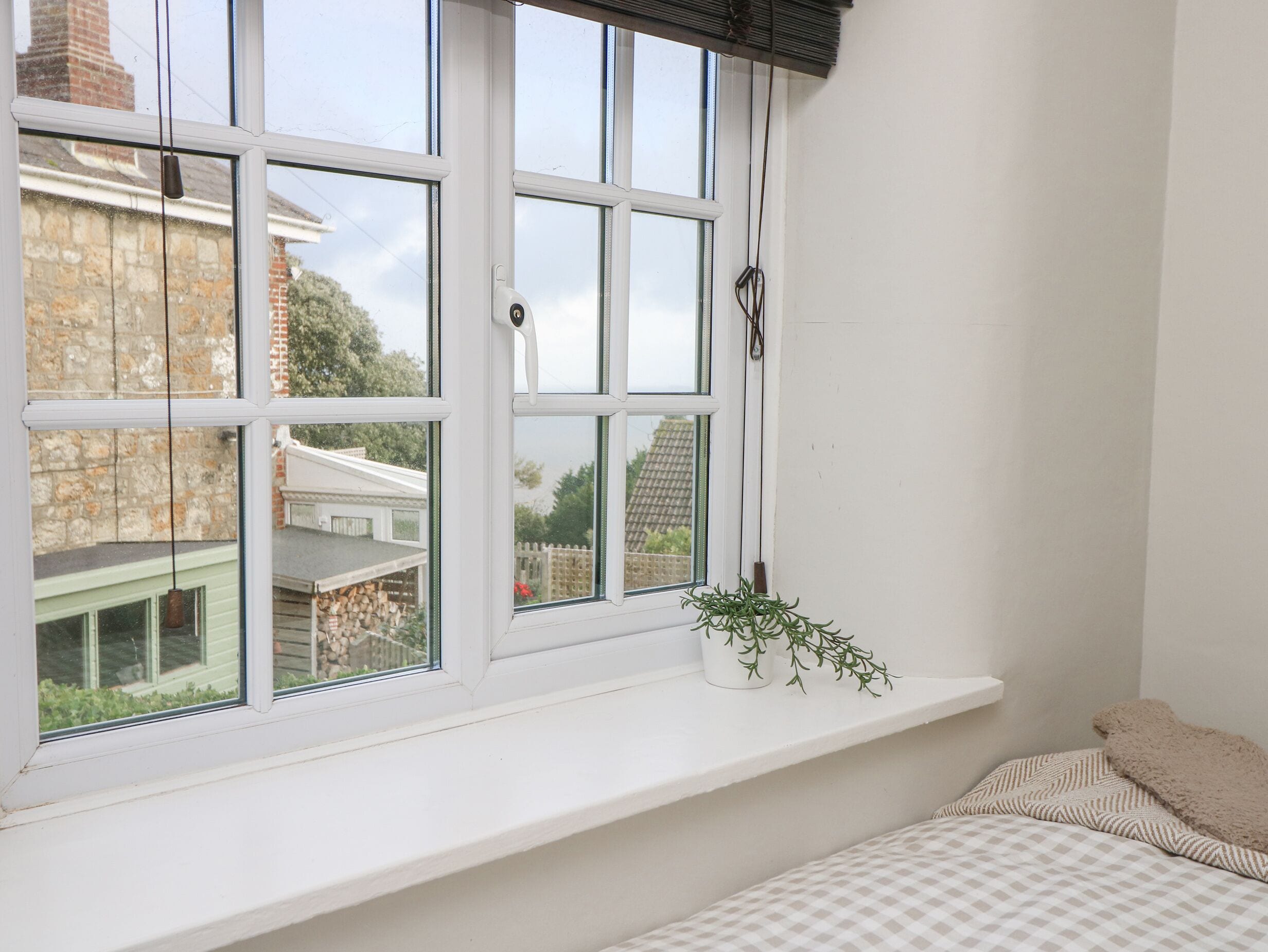 A bedroom with a large window, a white bedside table, and a bed with patterned bedding.