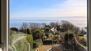 A view from a window overlooking a coastal landscape with a wooden deck, a house, and a clear sky. - Saltwater Cottage (Ventnor)