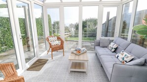 A conservatory with a grey sofa, wicker chairs, and a patterned floor. - Saltwater Cottage (Ventnor)