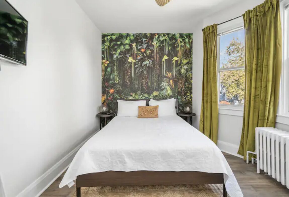 A bedroom with a bed, a wall mural, a window with curtains, and a radiator.