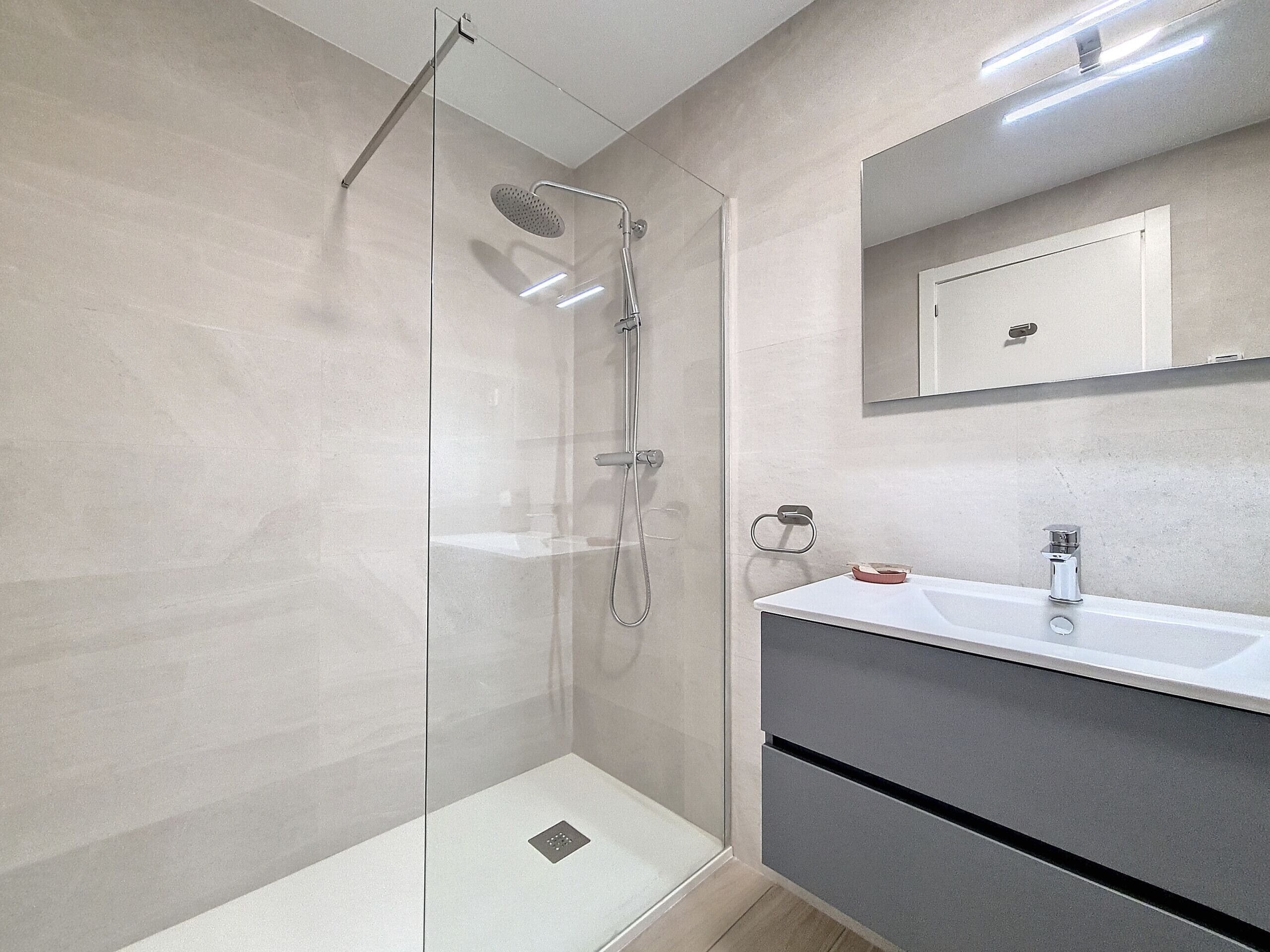 Ein modernes Badezimmer mit einer gläsernen Dusche, einem weißen Waschbecken und einem Spiegel darüber.
