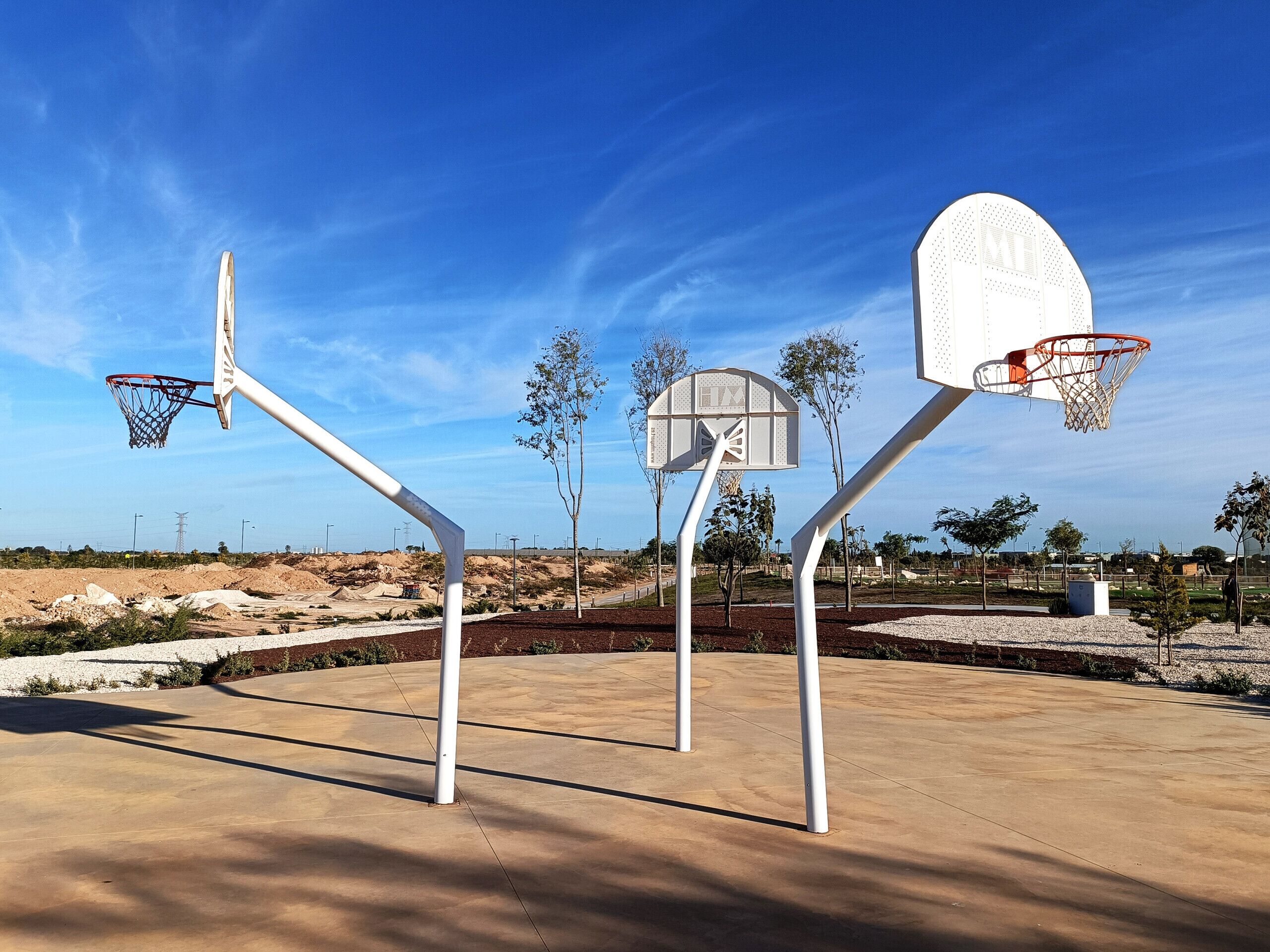 An outdoor basketball court with two hoops, surrounded by trees and a clear sky.