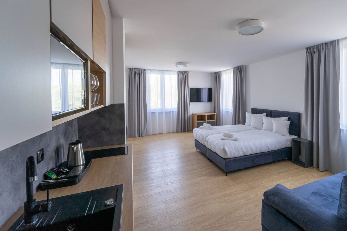 Et moderne hotelværelse med en stor seng, fjernsyn monteret på væggen, et skrivebord med stol og en sofa.