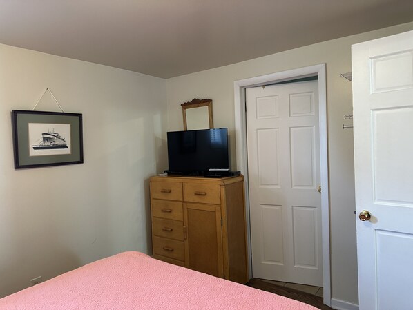 A bedroom with a bed, a dresser, a television on the dresser, a door, and a framed picture on the wall.
