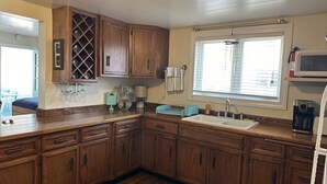 Una cocina con armarios de madera, una vinoteca integrada, un lavamanos y un ventanal con persianas.