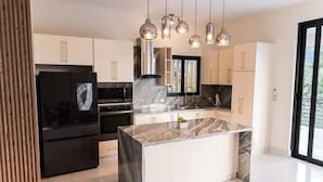 Una cocina moderna con una isla de mármol, electrodomésticos de acero inoxidable e iluminación colgante.