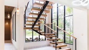 Una escalera moderna con escalones de madera y barandillas negras, que conduce a una habitación luminosa con ventanas amplias.