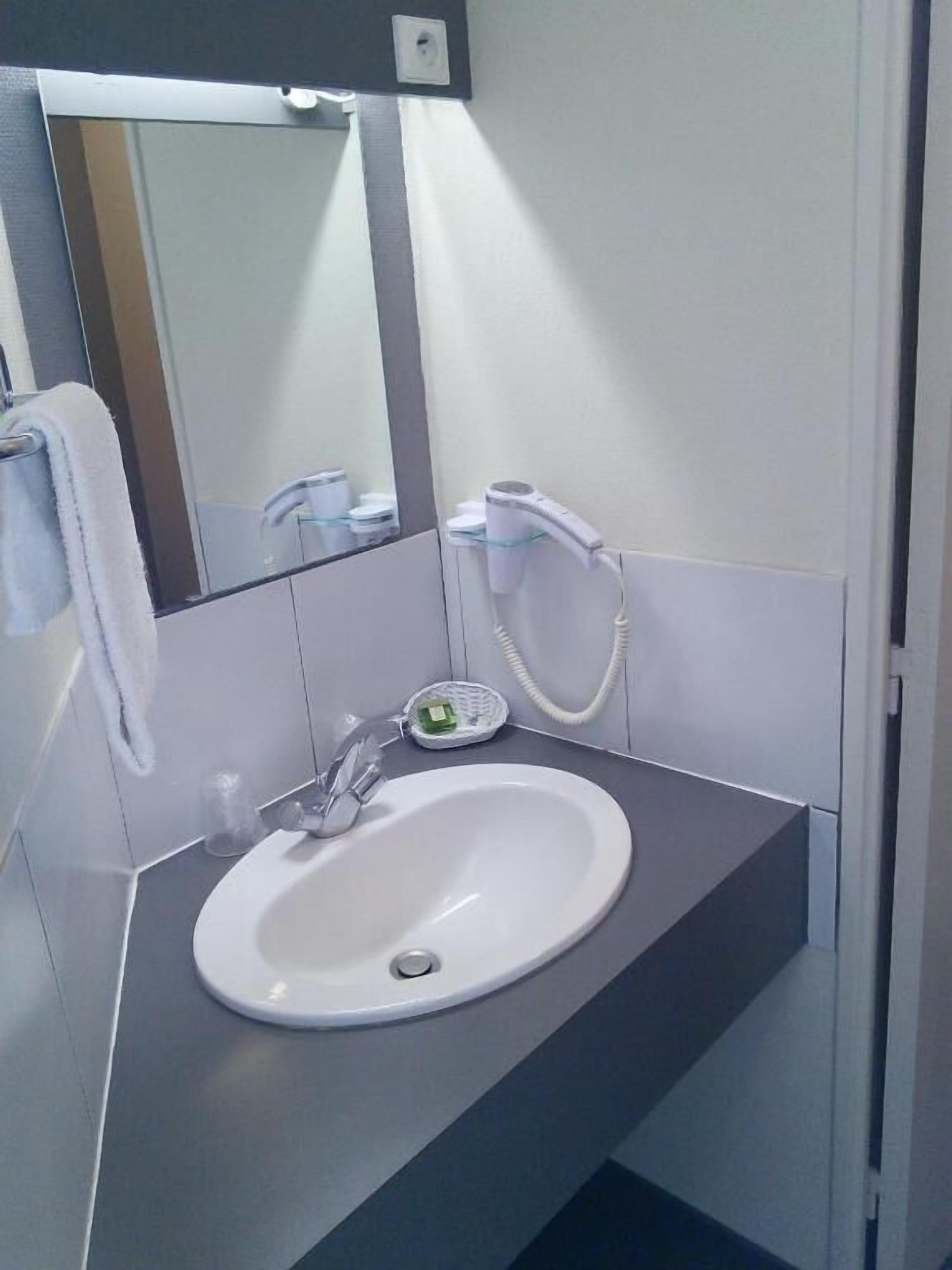 Un baño moderno con un lavamanos blanco, un espejo y un secador de pelo sobre un estante de vidrio.