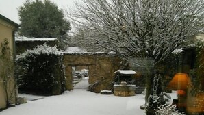 A snow-covered courtyard with a stone wall, a wooden bench, and a metal gate. - Hôtel du Commerce (Tronget)