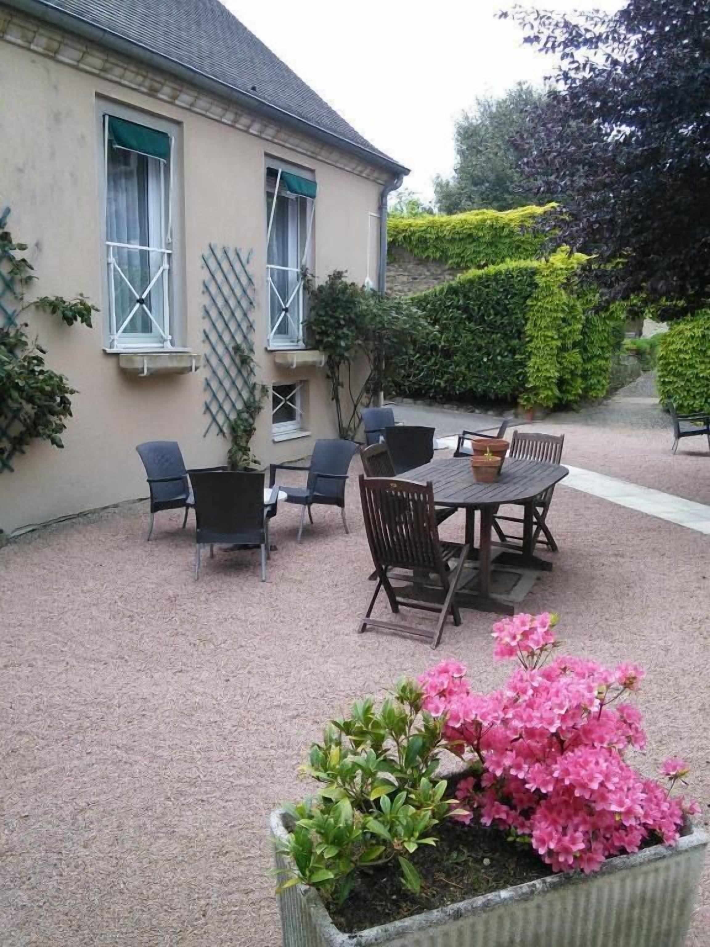 A patio with a table and chairs, a potted plant with pink flowers, and a building with windows and a lattice.
