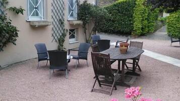A patio with a table and chairs, a potted plant with pink flowers, and a building with windows and a lattice.