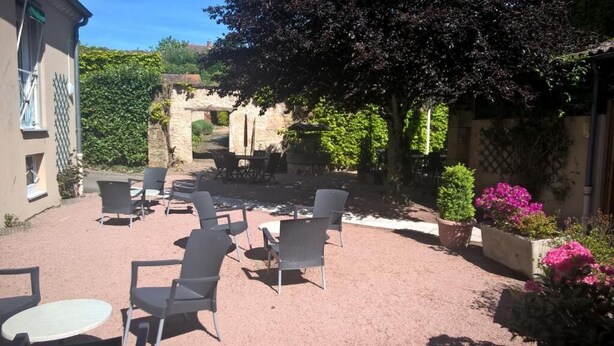 An outdoor patio with chairs and tables, surrounded by stone walls and greenery. - Hôtel du Commerce (Tronget)