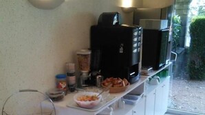 A breakfast setup with a checkered tablecloth, a fruit bowl, a coffee maker, and a microwave. - Hôtel du Commerce (Tronget)