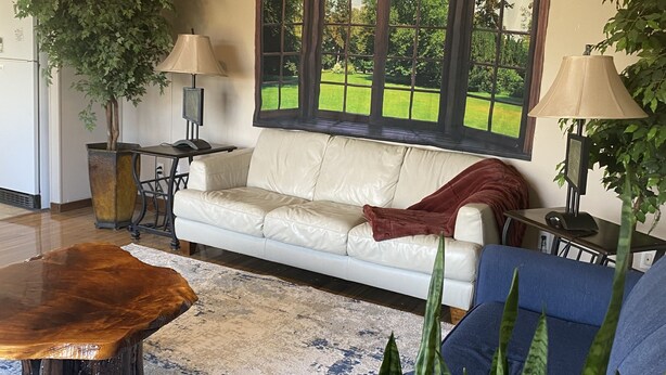 Ein Wohnzimmer mit einer Couch, einem Couchtisch und einem großen Fenster mit Blick auf eine grüne Landschaft.