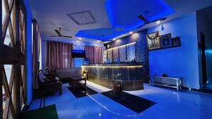 A modern hotel lobby with a reception desk, seating area, and a large window. - Raja residency near ISHA ADIYOGI ALANDURAI Siruvani Coimbatore ,Tamilnadu, India (Alanthurai)