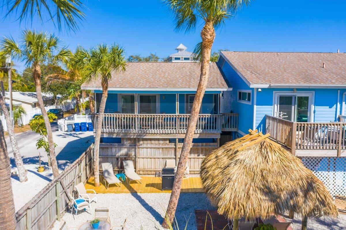 A two-story building with a balcony, palm trees, and a thatched umbrella.