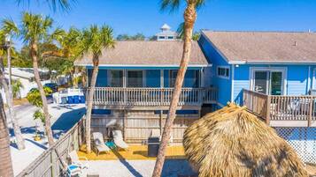 A two-story building with a balcony, palm trees, and a thatched umbrella.