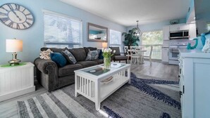 A living room with a sofa, coffee table, and a clock on the wall. - Siesta Shores: Shoreline Suite - King bed - Pool! (Sarasota)