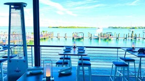 A dining area with tables and chairs, a candle, and a view of the water and dock. - Siesta Shores: Shoreline Suite - King bed - Pool! (Sarasota)