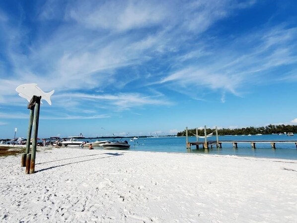 A beach with a wooden pier, boats, and a clear sky.
