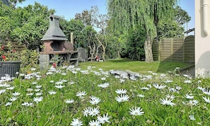A garden with a brick barbecue area, a lawn, and a variety of flowers.