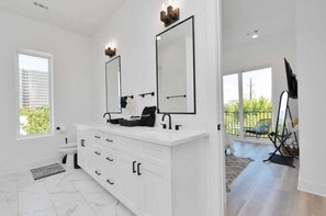Un baño moderno con un tocador blanco, dos espejos grandes y un ventanal con vistas al exterior.