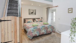 A bedroom with a large bed, a wooden door, a staircase, and a glass balcony.