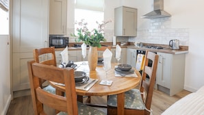 A modern kitchen with a dining table set for four, wooden chairs, a vase with flowers, and a stove.