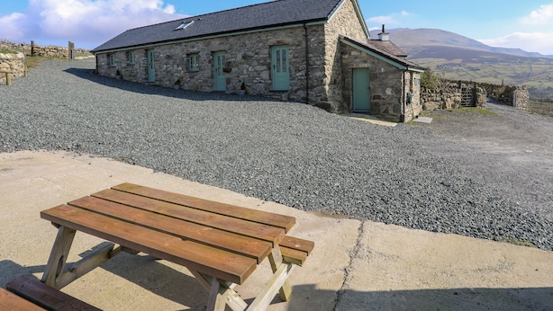 A stone building with a sloped roof, a gravel driveway, and a wooden picnic table.