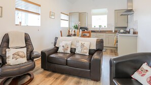 A modern living room with a brown leather sofa, a wooden dining table, and a kitchen in the background.
