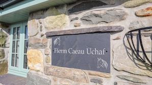 A stone wall with a sign that reads "Ferm Caeau Uchaf".