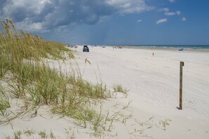 En strand med klitter, en træpæl og et par biler og mennesker i det fjerne.