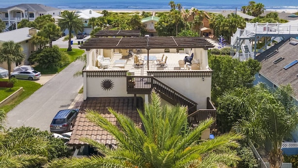 Ein zweistöckiges Haus mit einer Terrasse mit Blick auf den Strand, ausgestattet mit einem Sonnendesign an der Wand, einem überdachten Sitzbereich und Meerblick.