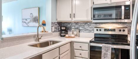 A modern kitchen with white cabinets, stainless steel appliances, and a tiled backsplash.