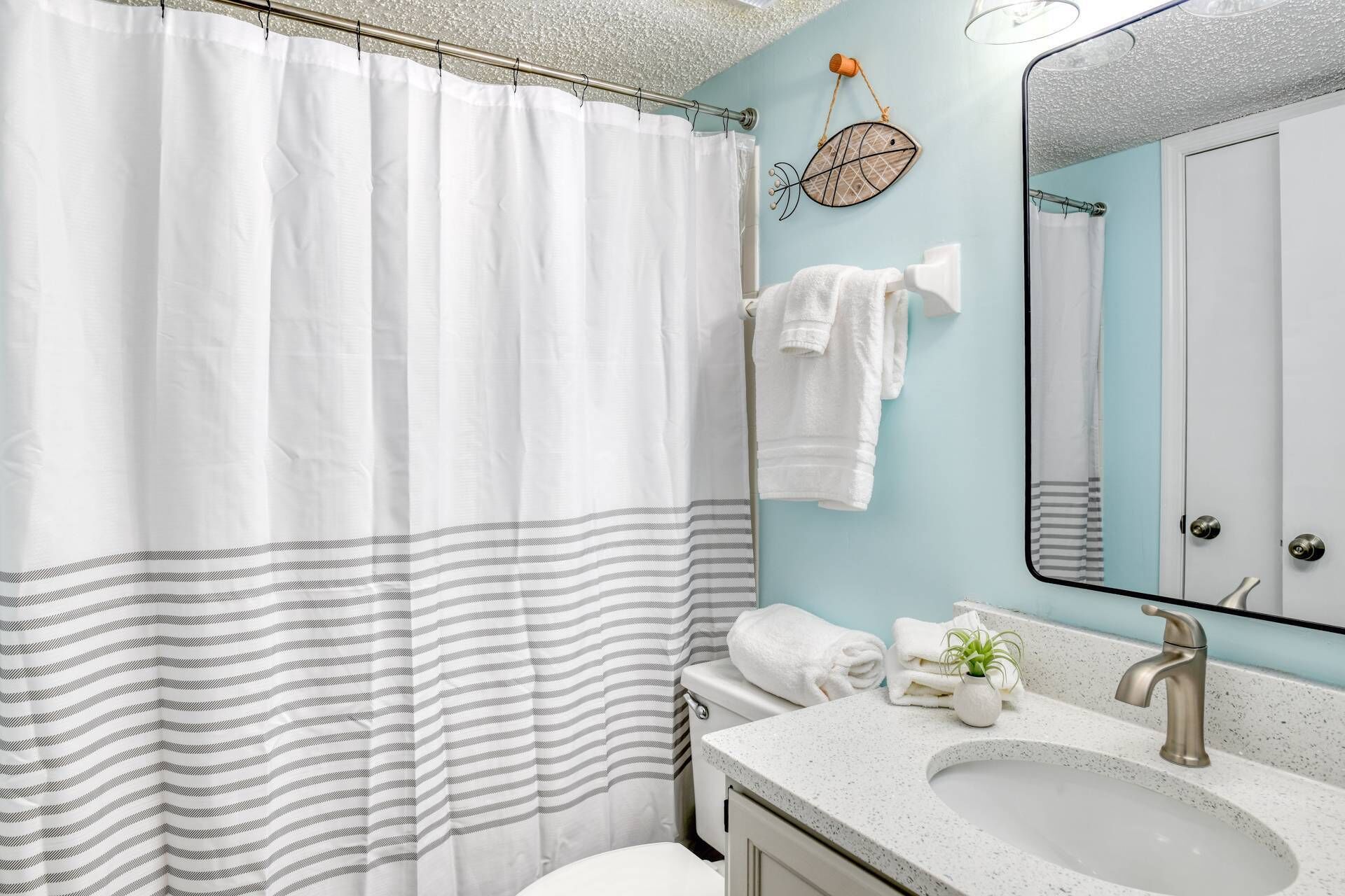 A bathroom with a striped shower curtain, a white towel, a small potted plant, and a sink with a mirror.