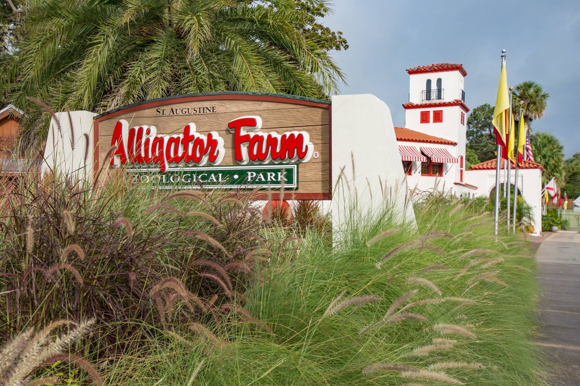Une enseigne indiquant l’emplacement d’une ferme aux alligators, un parc zoologique, avec un bâtiment aux couleurs rouge et blanc et un mât portant des drapeaux.