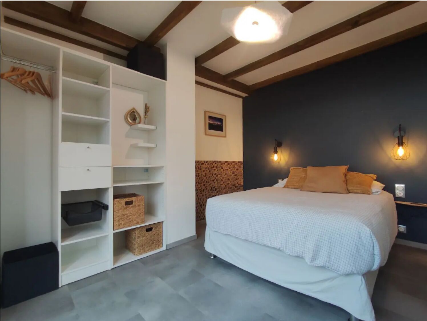 Une chambre à coucher avec un lit, une étagère blanche et un mur d’accent de couleur foncée.