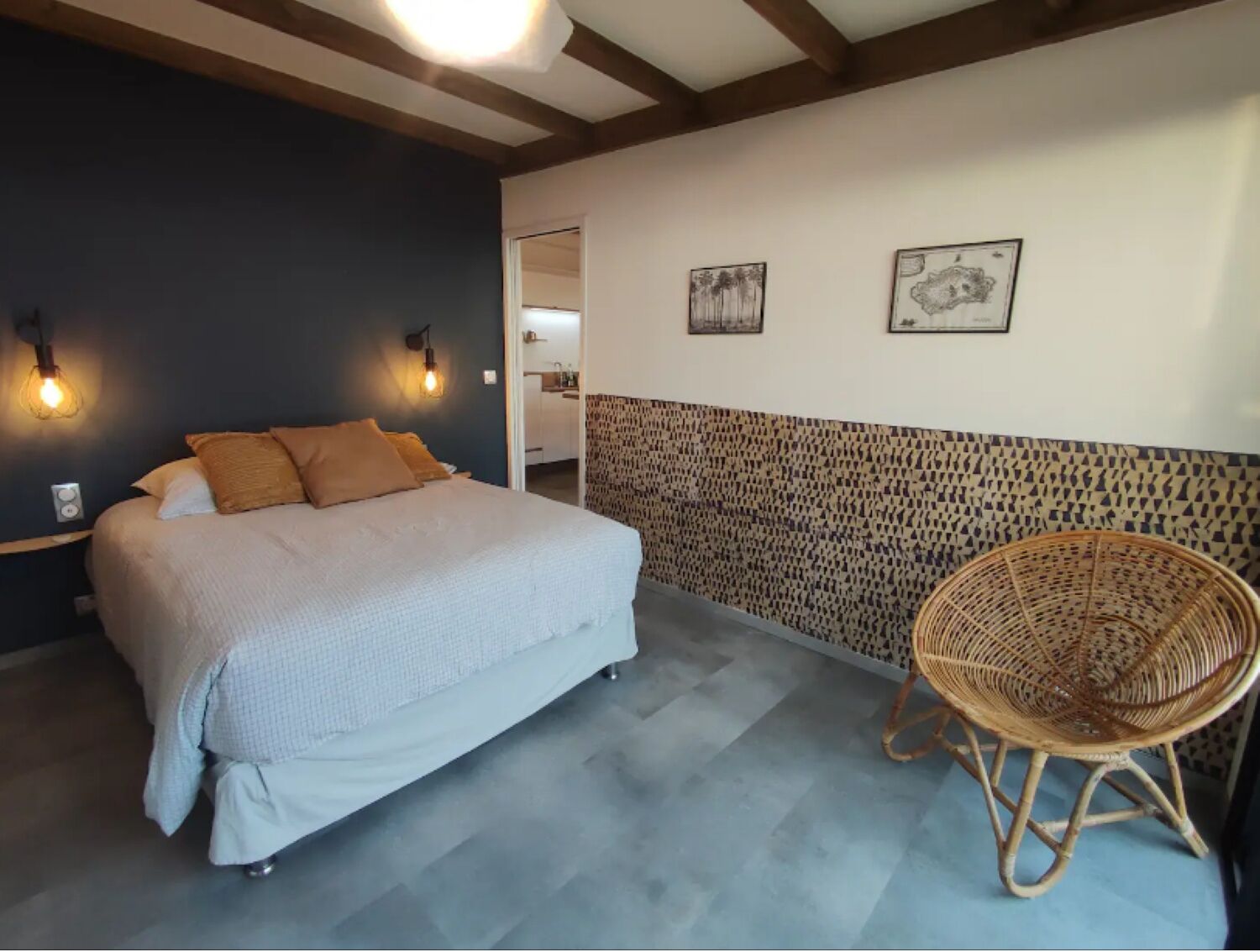 Ein Schlafzimmer mit einem Bett, zwei Wandleuchten, einem Korbstuhl und einer Wand mit Muster.
