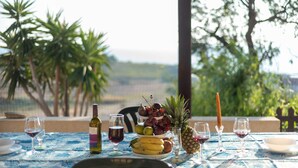 Une table dressée avec une bouteille de vin, des verres, un panier de fruits et une bougie, installée à l’extérieur, avec des arbres en arrière-plan.