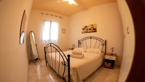 Une chambre à coucher avec un lit, une table de chevet, un miroir et un ventilateur de plafond.