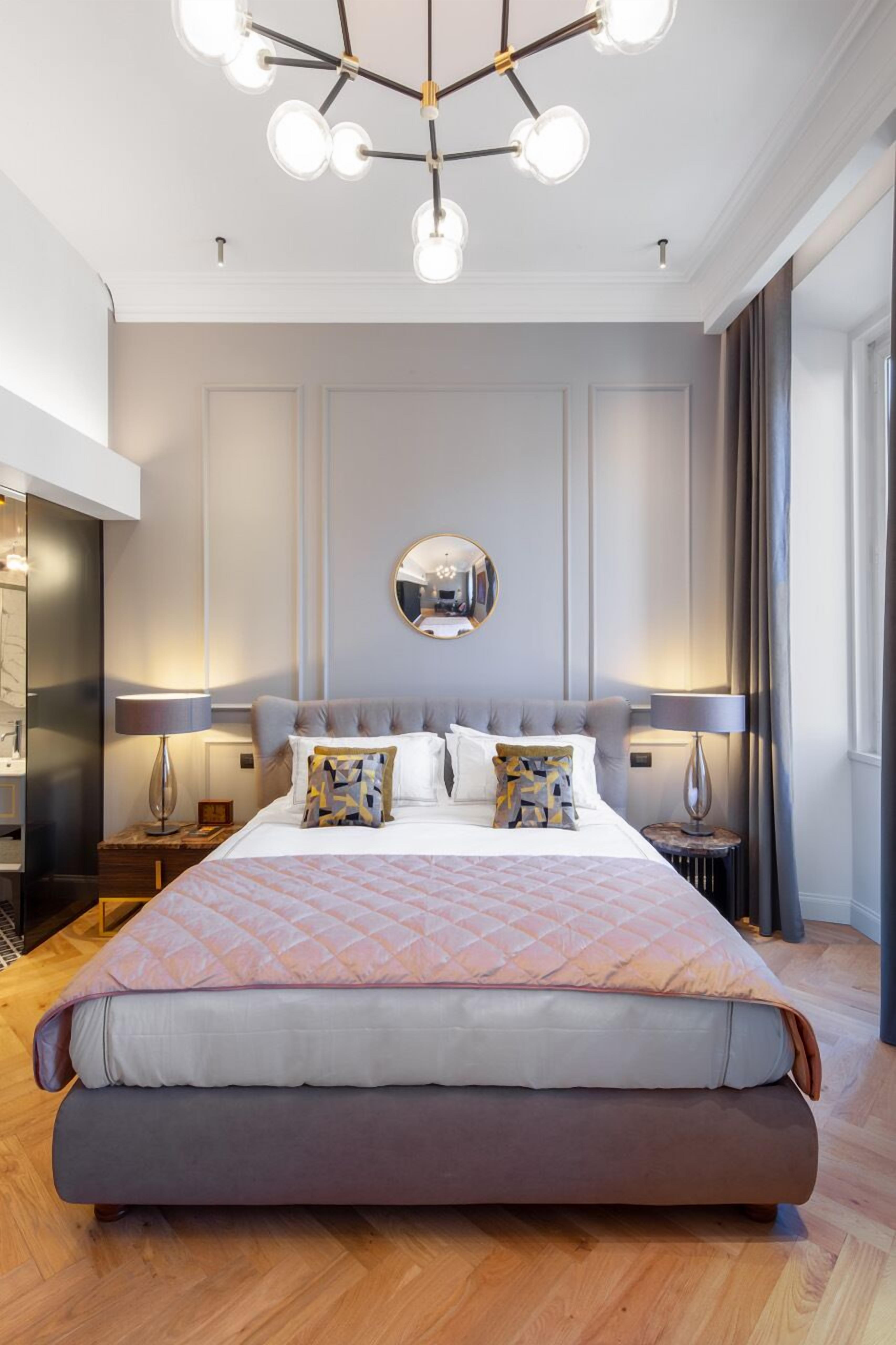 Un dormitorio moderno con una cama grande, dos mesitas de noche, un espejo y una lámpara de araña.