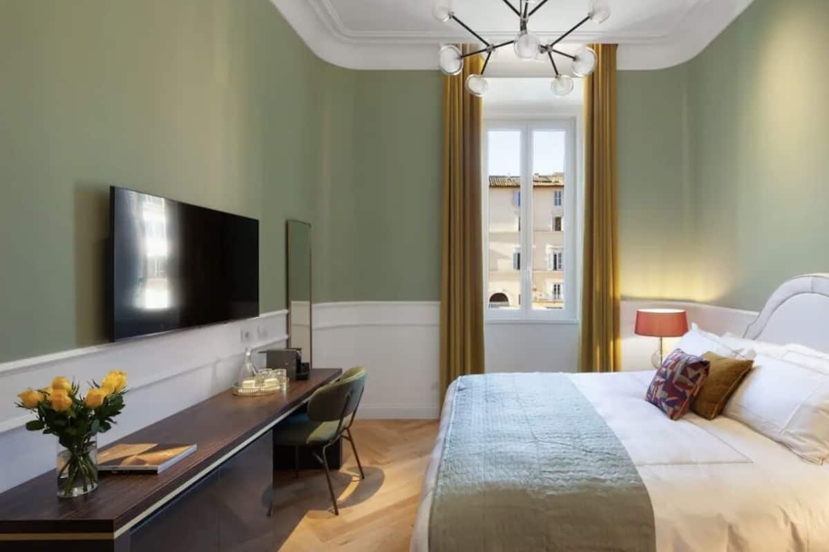 A hotel room with a bed, a desk with a chair, a television, and a window with curtains.