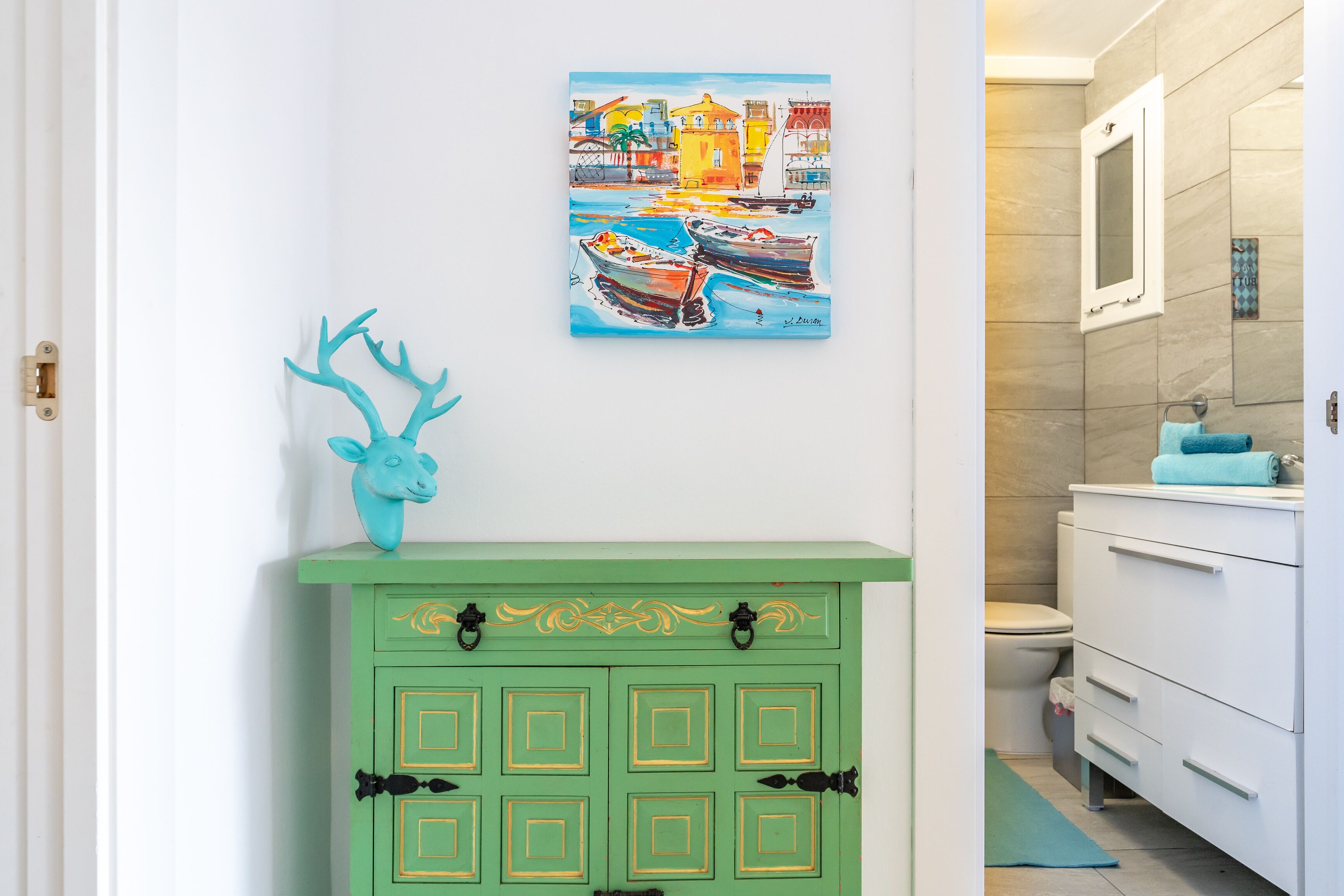 Un baño con un mueble verde, un tapete azul y un cuadro con barcos en la pared.