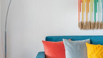 A modern living room with a blue sofa, colorful cushions, a floor lamp, and a decorative wall hanging.