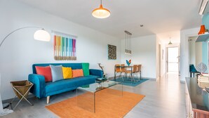 A modern living room with a blue sofa, a glass coffee table, and a dining area with a table and chairs. - Your Beach Front Retro Hideaway in Salou (Salou)