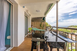 Ein Balkon mit Tisch und Stühlen, einer Hängematte, einem Ventilator und Blick auf das Meer.