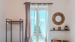 Une chambre avec un lit superposé, une fenêtre avec des rideaux, un miroir rond et une table de chevet agrémentée d’objets décoratifs.