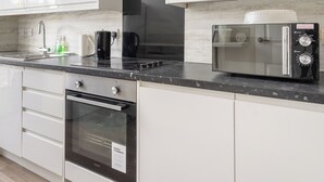 A modern kitchen with white cabinetry, a built-in oven, a microwave, and a coffee maker. - Stylish 2-Bed Flat in Edinburgh with Great Views (Edinburgh)